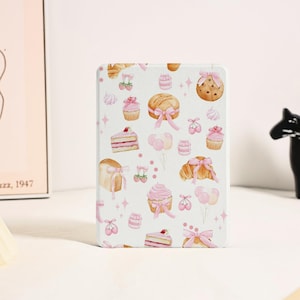 Puede incluir: Una funda rectangular para lector electrónico con fondo blanco y un patrón repetitivo de productos de repostería en tonos rosa, incluyendo cupcakes, trozos de pastel, cruasanes y galletas, decorados con lazos y globos rosas.