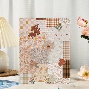 Pode incluir: Um diário decorativo com um design de patchwork. A capa apresenta vários padrões florais e geométricos em tons de bege, castanho e pêssego. O diário está em pé, mostrando seu design artístico único.