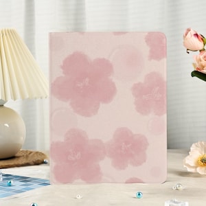 May include: A pale pink journal featuring a pattern of large, soft pink flowers. The cover has a watercolour effect, with the flowers overlapping. The background is a light pink. The journal is rectangular and appears to be closed.