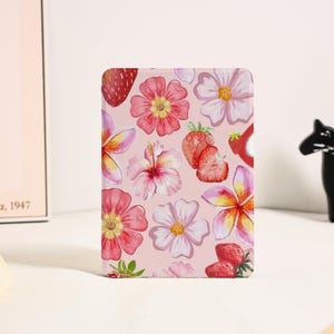 May include: A rectangular item with a floral pattern of pink flowers and strawberries on a light pink background. The design includes various flower types and sliced strawberries. The item is likely a notebook or stationery.