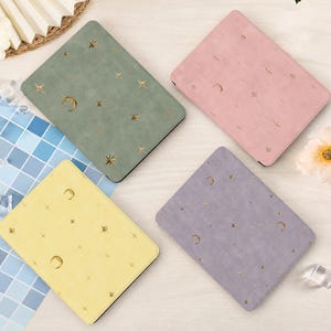 Può includere: Quattro quaderni rettangolari dai colori pastello. Ogni quaderno presenta un design celeste con lune e stelle dorate. I colori sono verde salvia, rosa, giallo e lavanda. I quaderni sono disposti su una superficie chiara.
