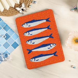 Puede incluir: Un posavasos rectangular naranja con cinco peces estilizados en azul y blanco. Los peces están dispuestos horizontalmente. Un artículo decorativo para proteger las superficies.