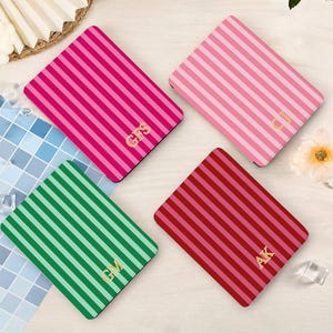 May include: Four rectangular cases featuring vertical stripes in shades of hot pink, light pink, green, and dark red. Each case is personalised with gold-coloured initials: GFS, CJ, GM, and AK, printed in a serif font on the lower right corner.