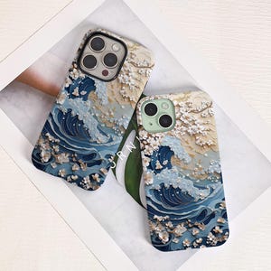 Puede incluir: Dos fundas para teléfono con un diseño de olas en tonos azules, beige y blanco. Las fundas presentan un efecto texturizado tridimensional con detalles florales. Las fundas están sobre una superficie blanca.