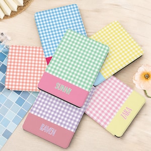 Pode incluir: Cinco estojos retangulares com padrão xadrez vichy em azul, amarelo, rosa, verde e roxo. Cada estojo tem uma seção inferior de cor sólida com um nome impresso em fonte simples: Sunny, Raven e Zara são visíveis em três dos estojos.