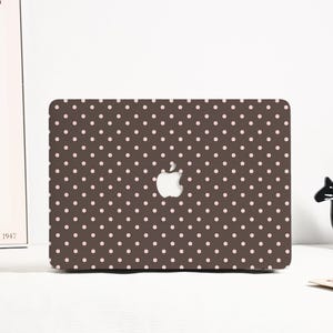 May include: A brown laptop case featuring a pattern of small, evenly spaced pink polka dots. The Apple logo is visible in the centre. The case is rectangular and covers the top of the laptop.