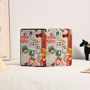 May include: A rectangular e-reader case featuring a collage of illustrations including a white rabbit, red cherries, strawberries, fish, and postage stamps. The design incorporates various cartoon characters and small graphic elements on a light background.