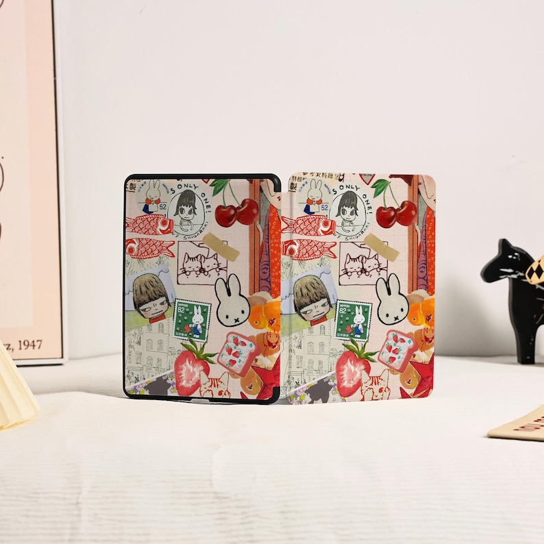 May include: A rectangular e-reader case featuring a collage of illustrations including a white rabbit, red cherries, strawberries, fish, and postage stamps. The design incorporates various cartoon characters and small graphic elements on a light background.
