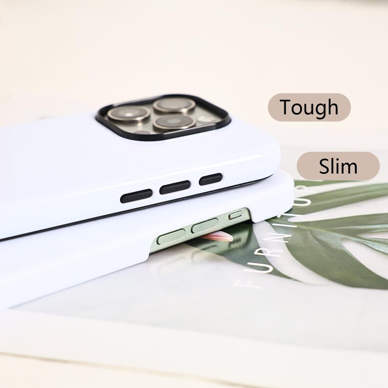 May include: Two white phone cases stacked on top of each other. The top case has a camera cutout with black trim and three lenses. The side of the case has black buttons. The text "Tough" and "Slim" are visible.