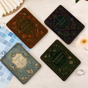 Op de afbeelding: Vier rechthoekige boeken met versierde covers. Linksboven een bruin boek met herfstbladeren getiteld Autumn Chronicles. Rechtsboven een donkerpaars boek met pauwen getiteld The Peacock Library. Linksonder een blauw boek met zeedieren getiteld Tides & Tales. Rechtsonder een groen boek met bloemmotieven getiteld Whispering Gardens.