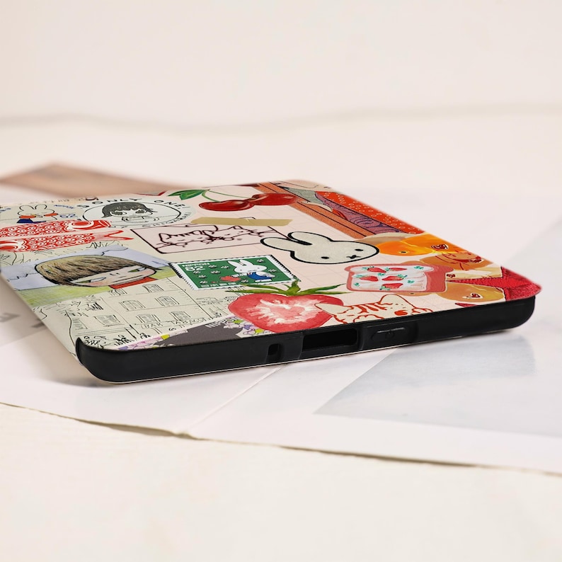 May include: A rectangular electronic device case featuring a collage of colorful illustrations including a white rabbit, red cherries, a sliced strawberry, a postage stamp, and a cartoon character with brown hair, all set against a cream background.