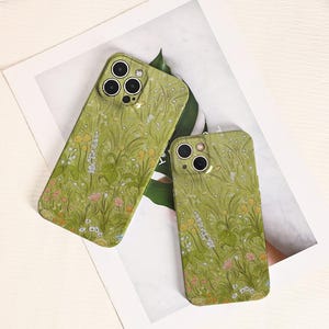 May include: Two green phone cases with a floral design featuring long blades of grass and colorful flowers. The cases have a matte finish and a camera cutout. The design is a repeating pattern of wildflowers.