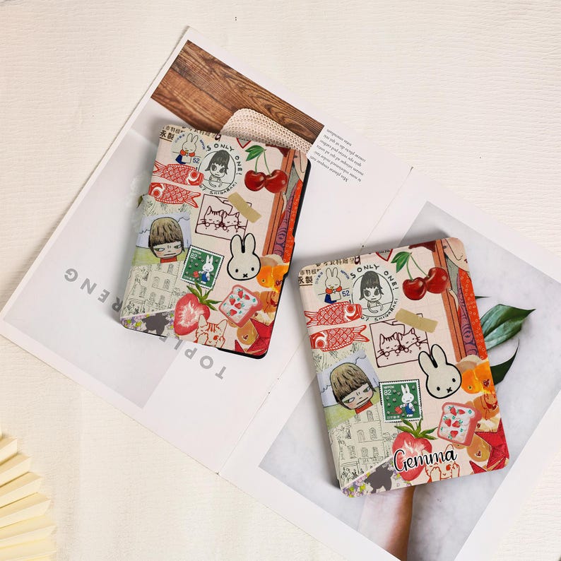 May include: Two rectangular e-reader cases featuring a collage of illustrations including a white rabbit, cherries, red fish, a person with short hair, and a green postage stamp. One case displays the name Gemma in cursive black script.
