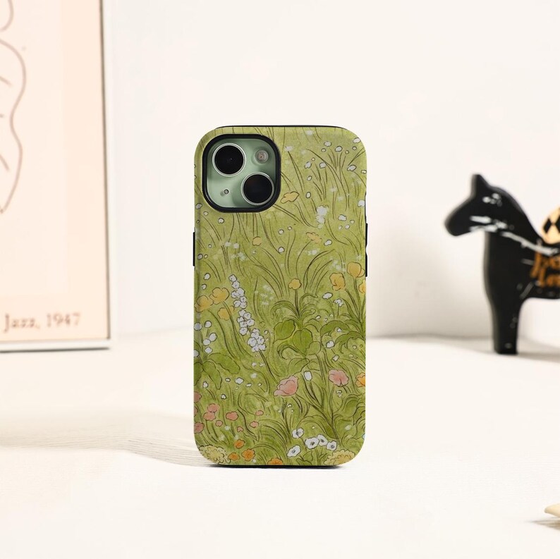 May include: A phone case with a floral design. The case features a green background with a pattern of wildflowers in shades of white, yellow, and pink. The phone case is designed to fit a smartphone.