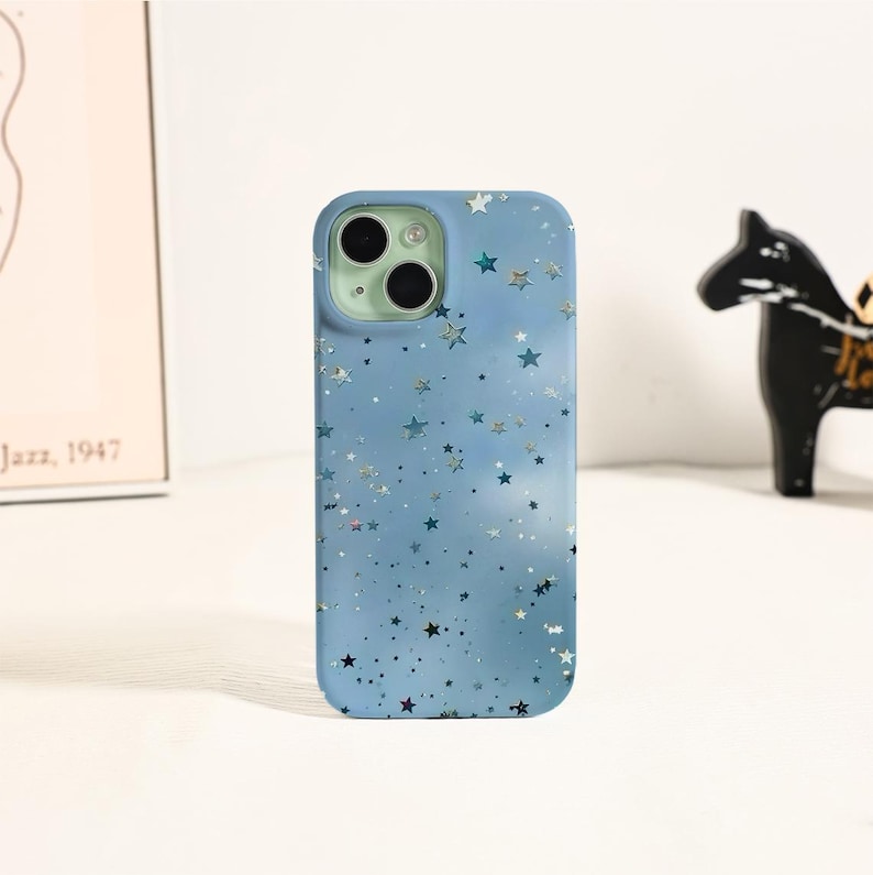 May include: A light blue phone case with a star pattern. The case has a matte finish and a camera cutout with three lenses. The stars are in various sizes and shades of blue and silver, creating a celestial design.