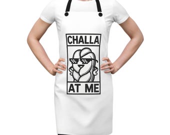 May include: White apron with a black and white illustration of a challah bread wearing sunglasses and the text "Challa at me".