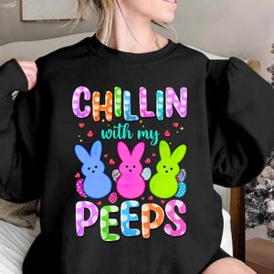 Puede incluir: Sudadera negra con un diseño gráfico colorido con tres peeps de dibujos animados y el texto "Chillin with my Peeps".