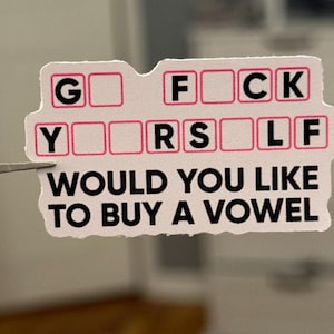 May include: A white sticker with the phrase "F*** Yourself" in a game show style, with blank spaces for letters. The text "Would you like to buy a vowel" is printed below the game show board.