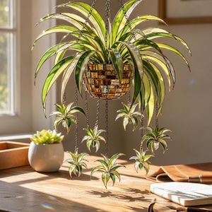 May include: A hanging stained glass plant sculpture featuring a central amber-toned mosaic pot with cascading green and white variegated leaves. Multiple smaller glass plant clusters are suspended from the main pot by thin metal chains.