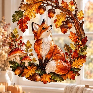 Peut inclure: Une décoration suspendue circulaire représentant un renard au centre, entouré d'éléments automnaux tels que des feuilles de chêne orange et brunes, des glands, des baies rouges et deux champignons, le tout dans un style vitrail translucide.