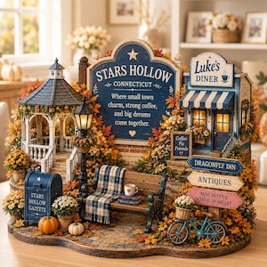 Pode incluir: Uma miniatura de Stars Hollow com um coreto, Luke's Diner, um banco de jardim com uma manta xadrez, uma caixa de correio azul com a inscrição Stars Hollow Gazette e placas para Dragonfly Inn, Antiques e Miss Patty's School of Ballet.