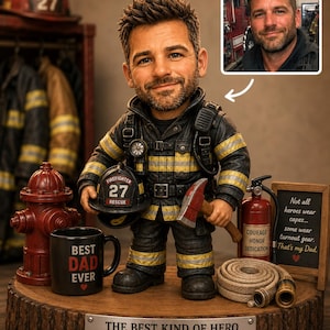 May include: A figurine of a firefighter holding a helmet and axe, with a mug that says "Best Dad Ever." The base has text that reads "The Best Kind of Hero Raises His Family Happy Father's Day!" A small photo is in the upper right.