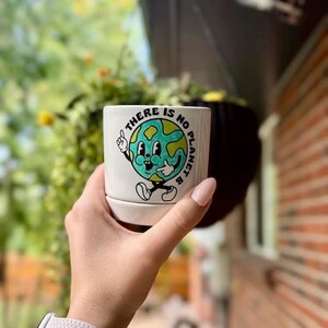 May include: White ceramic planter with a green and yellow cartoon earth illustration and the text "There is no planet B".