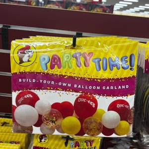 May include: A package of party supplies featuring a yellow and purple design with the words "PARTY TIME!" and "BUILD-YOUR-OWN BALLOON GARLAND." The package includes red, white, and yellow balloons. The Buc-ee's logo is visible.