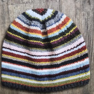 May include: A hand-knitted beanie hat with horizontal stripes in various colors, including blue, red, yellow, and gray. The hat is made of a soft, textured yarn and is suitable for cold weather. The beanie is a stylish accessory.