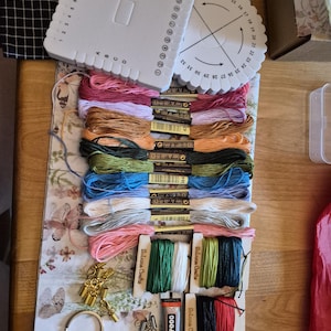 May include: A craft kit featuring a square and a round white plastic kumihimo braiding disk, multiple skeins of embroidery floss in various colors, three small spools of colored cord, gold-tone metal findings, a metal keyring, and a tube of B-7000 glue.