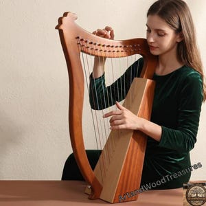 Puede incluir: Un arpa de madera con cuerdas, con un acabado marrón cálido. El arpa tiene un cuello curvado y una caja de resonancia rectangular. Las cuerdas son visibles y el instrumento está siendo tocado. La imagen está bien iluminada, mostrando los detalles del arpa.