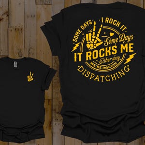 May include: Black t-shirt with a yellow graphic design featuring a skeleton hand making a peace sign. The graphic text reads "Some days I rock it. Some days it rocks me. Either way we're rockin' dispatching."