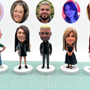 Könnte beinhalten: Eine Sammlung von individuellen Wackelkopf-Figuren, die jeweils eine Person mit einzigartiger Frisur und Kleidung darstellen. Die Figuren stehen auf weißen, kreisförmigen Sockeln. Darüber ovale Porträts der Personen.