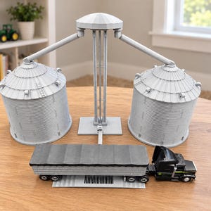 May include: A gray plastic toy grain elevator set featuring two cylindrical silos with corrugated textures, connected by a central support structure with overhead loading arms, positioned behind a black and gray toy semi-truck with a flatbed trailer.