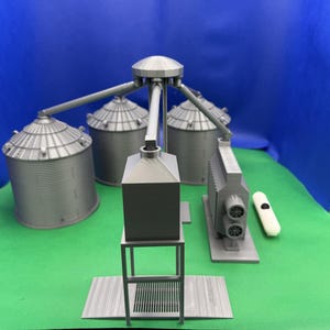 May include: A gray model of a grain silo with a series of pipes and a conveyor system. The silo has a tall, cylindrical shape with a domed top. The pipes and conveyor system are connected to the silo and extend out to the side. The model is made of plastic and is about 10 inches tall.
