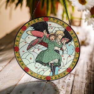 May include: Round stained glass window featuring a colorful anime scene with two characters. The design includes a green dress, wings, and a floral border with red roses. The window is hanging by a chain.