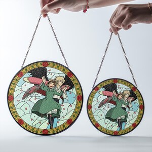 May include: Two round stained glass panels featuring a cartoon illustration of a couple with wings. The panels have a black border with a chain for hanging. The artwork includes a green dress, black wings, and a light blue background.