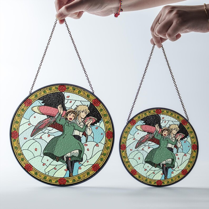 May include: Two round stained glass panels featuring a cartoon illustration of a couple with wings. The panels have a black border with a chain for hanging. The artwork includes a green dress, black wings, and a light blue background.