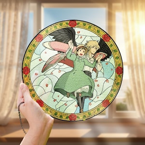 May include: Round stained glass art featuring a scene from an animated film. The artwork depicts two characters in a romantic embrace, surrounded by a floral border with red roses. The background is a light blue sky with scattered rose petals.
