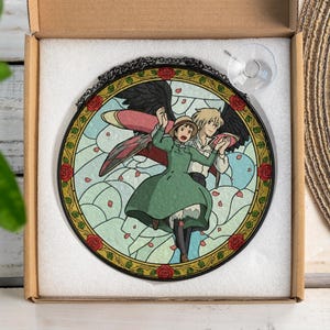 May include: Round stained glass window featuring a couple dancing, with a black border and red rose accents. The artwork depicts a scene with a green dress and a light blue sky background. Includes a suction cup for hanging.