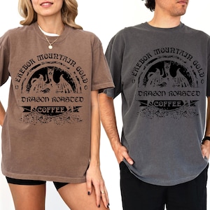 May include: Two people wearing brown and gray t-shirts with a black graphic print of a dragon and the text "Erebor Mountain Gold Dragon Roasted Coffee".