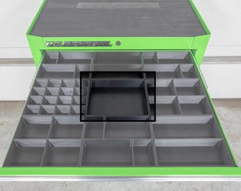 May include: A green and gray tool chest with an open drawer revealing a black tray insert. The drawer is divided into multiple compartments of varying sizes. The tool chest has the text "U.S. GENERAL" on the top.