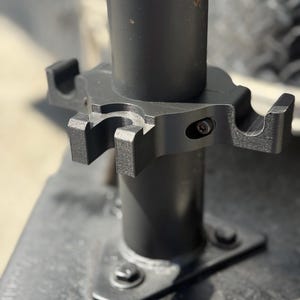 May include: Close-up of a black metal bike rack with a silver screw. The rack is attached to a black metal pole.