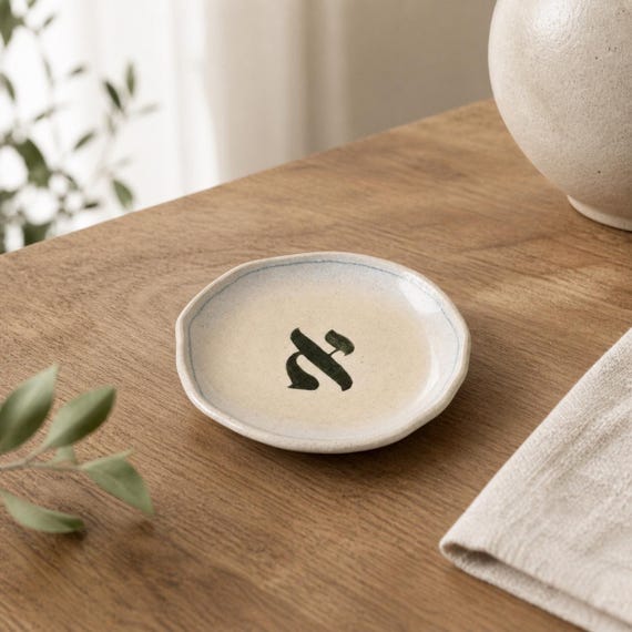 A handmade ceramic trinket bowl stamped with a Hebrew letter — quietly meaningful Judaica that doubles as everyday desk/vanity decor.