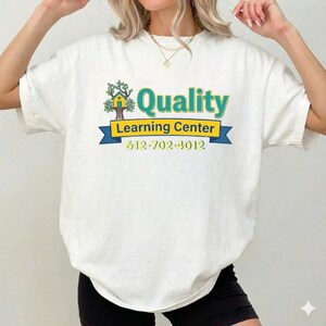 May include: White t-shirt with a colorful graphic for a learning center. The design includes the word "Quality" in teal, a tree and house icon, and the text "Learning Center" with a phone number.