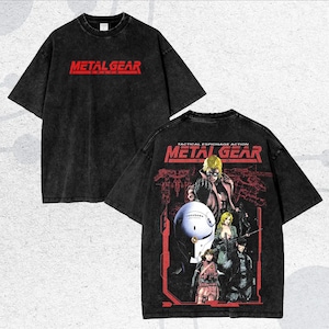 May include: Dark grey t-shirt displaying the red text "METAL GEAR". The back of the tee features a graphic with the text "TACTICAL ESPIONAGE ACTION METAL GEAR" and a detailed illustration of characters and a futuristic setting.