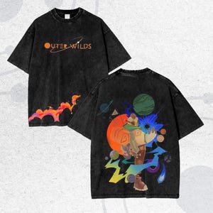 Puede incluir: Camisetas negras con el texto "Outer Wilds" en naranja. La parte delantera de la camiseta tiene un diseño naranja y rosa. La parte trasera de la camiseta tiene un diseño gráfico colorido con planetas, formas geométricas y una figura.