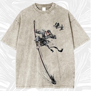 Op de afbeelding: Een steen-gewassen T-shirt met korte mouwen met een dynamische illustratie van een figuur met een staf. Het kunstwerk is in zwarte en rode inkt, met Chinese karakters boven de figuur. Het shirt heeft een ronde hals en een relaxte pasvorm.