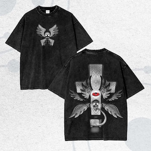 Peut inclure: Deux t-shirts noirs avec un aspect vieilli. L'un présente un motif de crâne ailé sur le devant. L'autre affiche un motif de croix au dos, avec un œil, des ailes et un serpent.