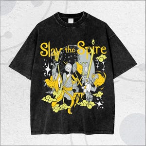 May include: Black t-shirt with a graphic design featuring the text "Slay the Spire" in yellow. The design includes cartoon figures with staffs and a moon background. The shirt has a vintage, washed look.